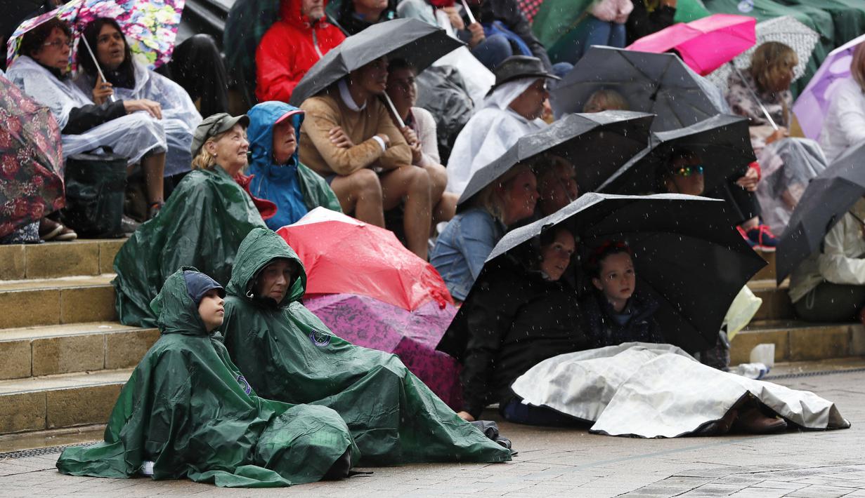Penonton menggunakan jas hujan dan payung saat menyaksikan pertandingan antara Johanna Konta melawan Simona Halep pada perempat final tunggal putri Wimbledon 2017 di The All England Lawn Tennis Club, London, (11/7/2017). (AP/Kirsty Wigglesworth)