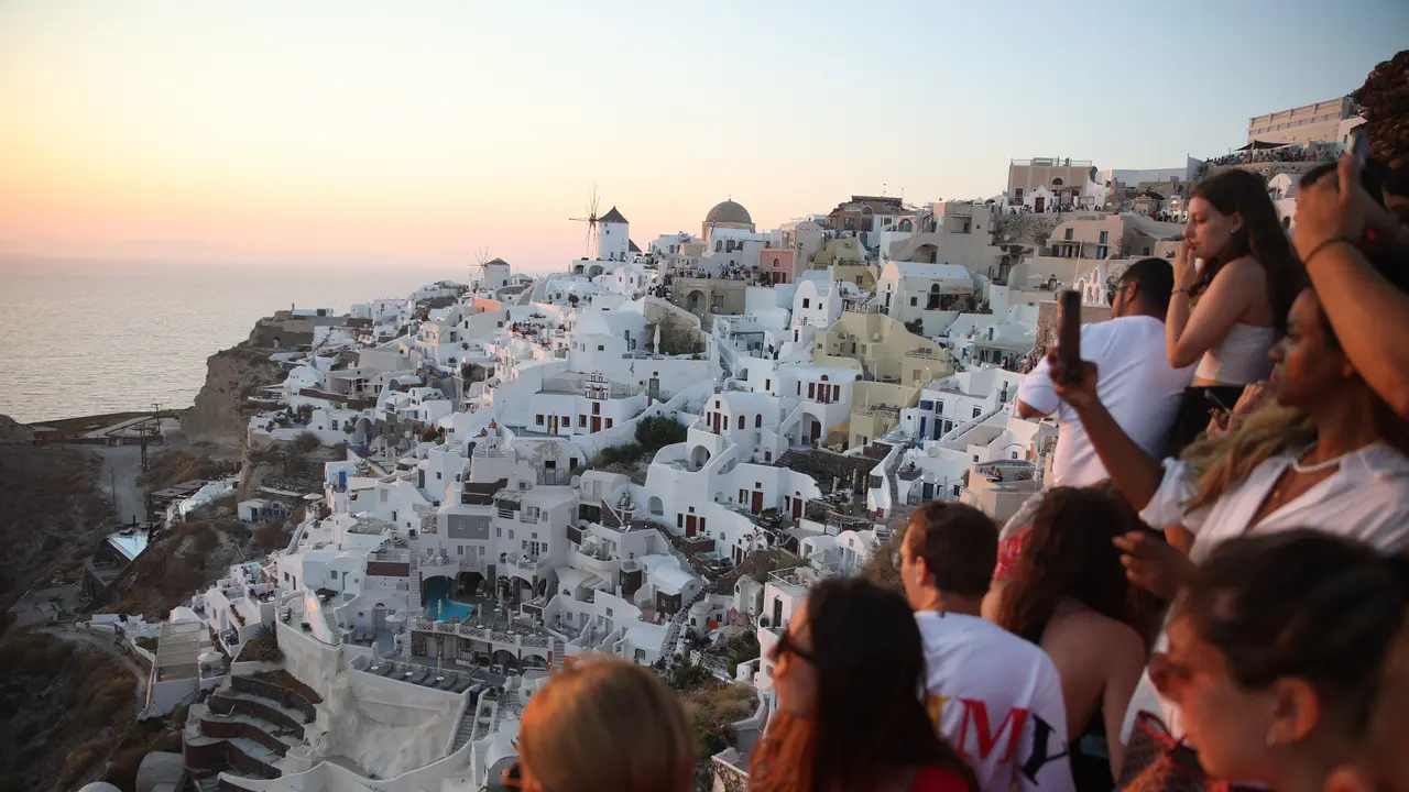 Turis menunggu matahari terbenam di desa Oia di pulau Santorini, Yunani, pada 20 Juli 2024. Seperti destinasi wisata populer lainnya, pulau Cycladic yang bertengger di atas gunung berapi itu mendekati titik jenuh, dan kini ingin membatasi jumlah kapal pes