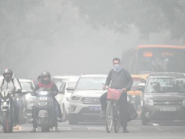 Seorang pengendara sepeda dengan wajah ditutupi masker melintasi sebuah jalan di pagi hari yang dingin dan berkabut di New Delhi pada tanggal 18 November 2024. (Money SHARMA/AFP)