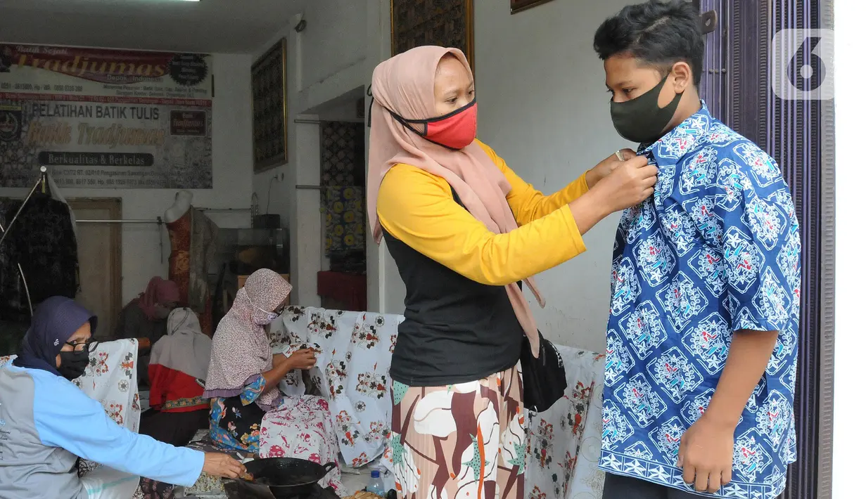 Seorang ibu mencoba ukuran baju seragam batik untuk anaknya di sentra batik Depok Tradjumas, Kamis (24/2/2022). Produksi Batik Depok kembali menggeliat pasca diberlakukannya pembelajaran tatap muka (PTM) di mana murid SD dan SMP menggunakan seragam batik produksi mereka. (merdeka.com/Arie Basuki)