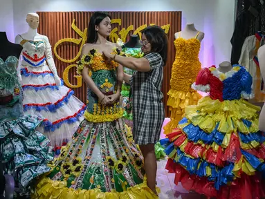 Dalam foto yang diambil pada tanggal 12 September 2024 ini, Leonora Buenviaje (kanan) menyiapkan gaun yang terbuat dari bahan daur ulang untuk Maria Theresa Deligero (kiri), di rumahnya di Cainta, provinsi Rizal, Filipina. (JAM STA ROSA/AFP)