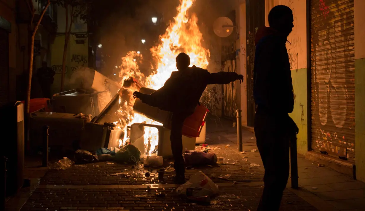 Pengunjuk rasa membakar sampah setelah kematian seorang pedagang kaki lima di distrik Lavapies di Madrid (15/3). Pedagang bernama Mmame Mbage diduga tewas setelah dikejar-kejar aparat kepolisian. (AFP Photo/Olmo Calvo)