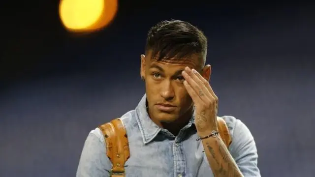 Neymar yang absen karena cedera gagal bersembunyi di balik jas hujannya saat hadir di tengah penonton memberi dukungan pada Barcelona di Liga Champions melawan Bayer Leverkusen.