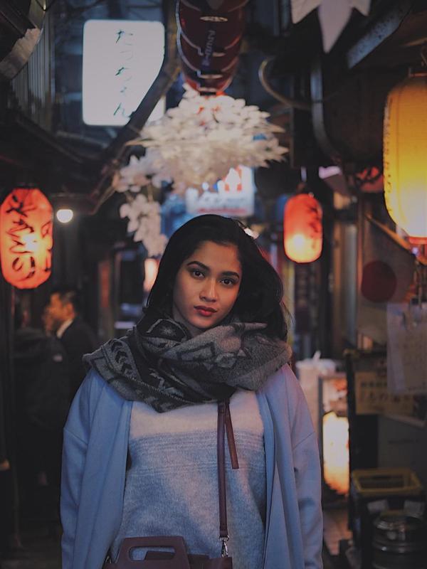 Berpose di jalanan Tokyo dengan latar lampion di depan kedai khas Jepang, wanita kelahiran tahun 1997 ini menggunakan busana berwarna tenang. Kali ini syal berwarna abu-abu bermotif gelap melindungi lehernya dari kedinginan. (Liputan6.com/IG/@aghninyhaque)