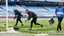 Petugas bahu membahu untuk membersihkan salju yang menutupi rumput jelang laga Manchester City melawan PSG pada laga semifinal Liga Champions di Stadion Etihad, Rabu (5/5/2021). (AFP/Paul Ellis)