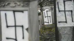 Sejumlah batu nisan dan monumen Holocaust yang dicoret-coret dengan simbol swastika nazi di sebuah pemakaman Yahudi di Strasbourg, Prancis (17/12). Aksi vandalisme ini diketahui dilakukan Selasa di pemakaman Yahudi Herrlisheim. (AFP Photo/Sebastien Bozon)