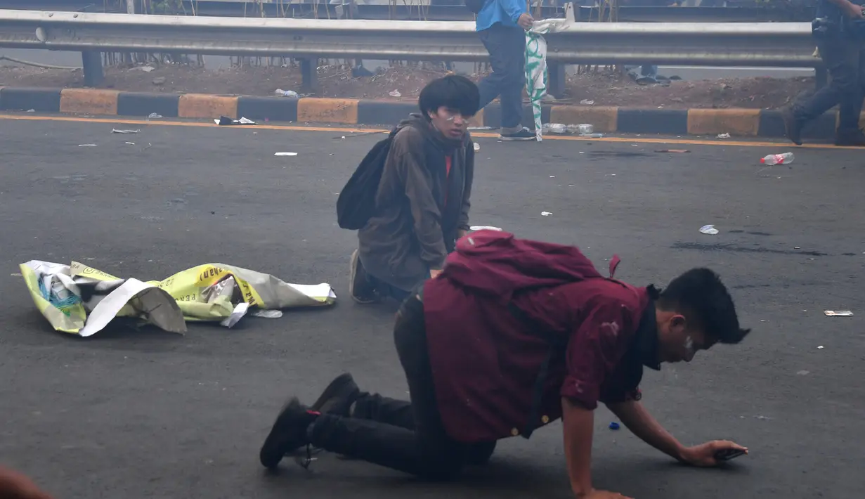 Mahasiswa tersungkur saat mencoba melarikan diri dari tembakan gas air mata aparat kepolisian dalam demonstrasi menolak pengesahan RUU KUHP dan revisi UU KPK di depan Gedung DPR, Jakarta, Selasa (24/9/2019). Sejumlah mahasiswa tumbang setelah polisi menembakkan gas air mata. (ADEK BERRY/AFP)