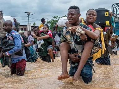 Warga menggendong seorang perempuan sementara lainnya menyeberangi banjir di distrik Ndjili, Kinshasa, pada 6 April 2025. (Hardy BOPE/AFP)