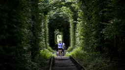 Seorang wanita dan pria berjalan di sepanjang bekas rel kereta api atau disebut 'Tunnel of Love' dekat desa Ukraina Klevan, Rivno, (6/8). Terowongan ini menjadi tempat bagi wisatawan dan pasangan yang sedang jatuh cinta. (AFP Photo/Sergei Supinsky)