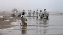 Petugas kebersihan bekerja untuk mengeluarkan minyak dari Pantai Cavero di Callao, Peru, 26 Januari 2022. Pembersihan Pantai Cavero dari tumpahan minyak kapal tanker Mare Doricum yang dihantam gelombang akibat letusan gunung berapi Tonga masih terus dilakukan. (Cris BOURONCLE/AFP)