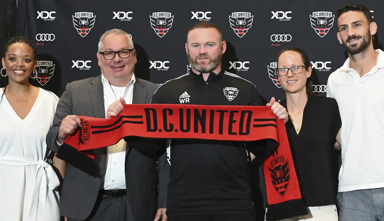 Wayne Rooney (tengah) berfoto bersama jajaran staff, manajemen dan pemain saat diperkenalkan sebagai pelatih baru DC United dalam konferensi pers di Audi Field, Washington (12/7/2022). Wayne Rooney saat ini tengah membesut DC United sejak ditunjuk pada 12 Juli 2022. Sebelumnya ia sempat menangani Derby County mulai 14 November 2020 hingga 24 Juni 2022. (AFP/Roberto Schmidt)