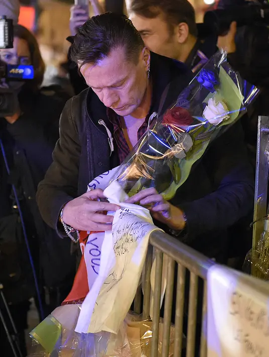 Bassist grup band U2, Adam Clayton meletakkan karangan bunga di trotoar di depan gedung pertunjukan Bataclan Theatre, salah satu tempat serangan teroris di Paris, Perancis, Sabtu (14/11). (AFP PHOTO / FRANCK FIFE)