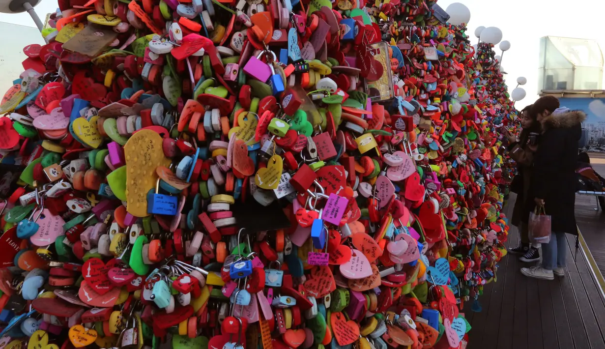 Sepasang pengunjung mengamati gembok cinta yang menutupi pagar di Namsan Seoul Tower, Korea Selatan, Selasa (29/1). Mitosnya, pasangan yang mengaitkan gembok cinta dan membuang kuncinya ke bawah akan menjadi pasangan abadi. (AP/Ahn Young-joon)