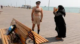 Seorang istri mengambil gambar suaminya di tepi laut, Pulau Kish di Iran, 1 November 2016. Di sini, laki-laki masih diperbolehkan mengenakan celana pendek dan jarang terlihat ada polisi syariat. (Atta Kenare/AFP)