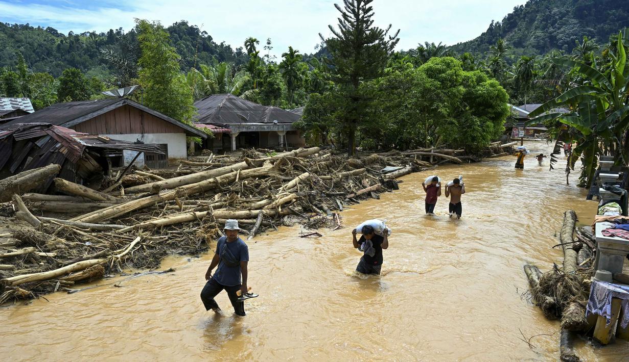 Hingga saat ini listrik masih padam di Tapanuli Tengah dan akses internet masih terbatas menggunakan Starlink, termasuk Bahan Bakar Minyak (BBM) hingga gas elpiji. Tampak dalam foto, warga berjalan di tengah banjir bandang di Desa Tukka, Tapanuli Tengah, Sumatera Utara, pada 2 Desember 2025. (YT HARIONO/AFP)