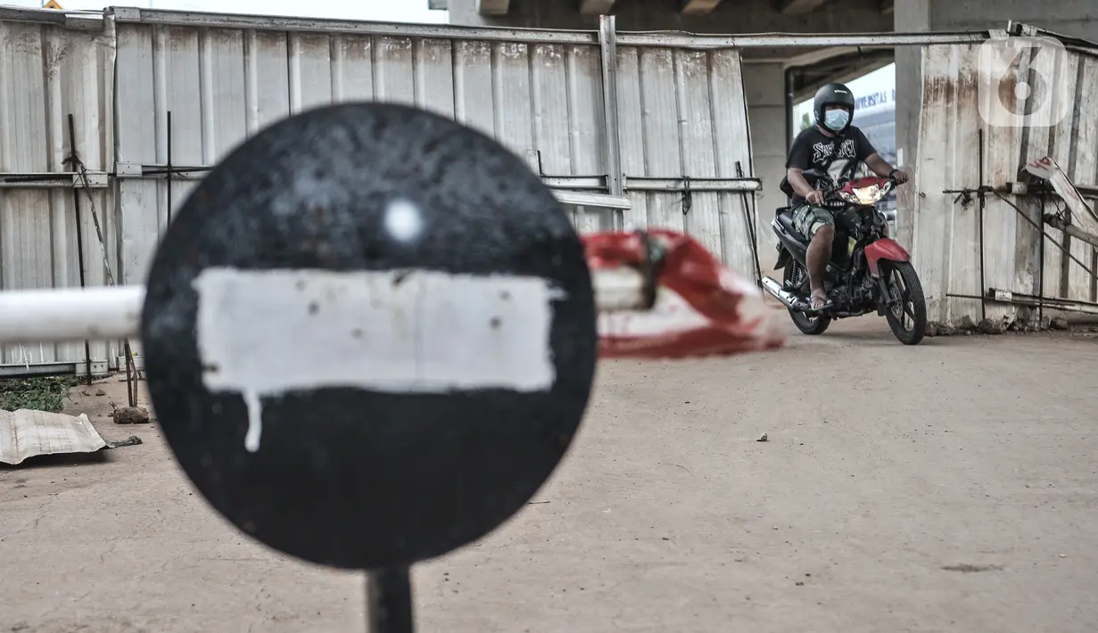 Pengendara sepeda motor melintasi pembatas yang dipasang di depan wilayah zona merah Covid-19 di RW 004, Cipinang Melayu, Jakarta, Rabu (27/1/2021). Pemprov DKI Jakarta mencatat sebanyak 54 rukun warga (RW) menjadi zona merah Covid-19 per 21 Januari 2021. (merdeka.com/Iqbal S Nugroho)