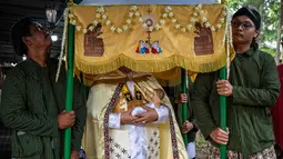 Gereja Hati Kudus Yesus ini dikenal memiliki ciri khas yakni memadukan unsur budaya lokal dalam setiap perayaan keagamaan. Tampak dalam foto, umat Katolik membawa patung bayi Yesus sambil menunggu Misa Malam Natal di Gereja Hati Kudus Yesus di Ganjuran, Bantul, Yogyakarta, pada Rabu 24 Desember 2025. (DEVI RAHMAN/AFP)