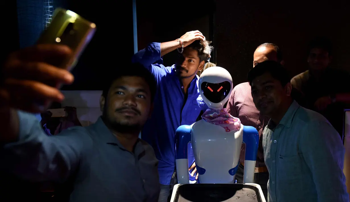 Pengunjung berselfie dengan pelayan robot di restoran bertema robot di Chennai, India (20/12). Restoran ini merupakan yang pertama di India yang memiliki pelayan robot dengan server otomatis membawa piring dari dapur ke pelanggan. (AFP Photo/Arun Sankar)