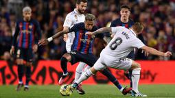 Pemain Barcelona, Raphinha (tengah) berusaha melewati pemain Real Madrid pada laga pekan ke-26 Liga Spanyol 2022/2023 di Camp Nou, Barcelona, Senin (20/03/2023). Blaugrana menang dengan skor 2-1 pada pertandingan yang bertajuk El Classico tersebut. (AFP/Josep Lago)