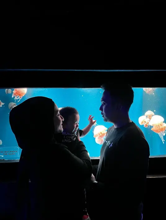 Nathalie Holscher yang menggendong baby Adzam berhadapan dengan Fariz Utama dilatari aquarium kaca yang tampak dari depan serupa persegi panjang. Diunggah di akun Instagram pribadi, 6 November 2022, Fariz Utama menulis pesan ringkas tapi bikin netizen baper, “PS I love you.” Nathalie Hoslcher merespons di kolom komentar, “PS mainan, By? (Foto: Dok. Instagram @farizutama30)