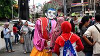 Foto pada 16 Maret 2019 menunjukkan ondel-ondel yang dioperasikan oleh seorang anak untuk mengamen di jalanan Jakarta. Seiring berjalan waktu, ondel-ondel yang dahulu sebagai ikon kesenian Betawi kini mudah ditemui di sejumlah jalan dan gang-gang di antara permukiman warga. (GOH CHAI HIN / AFP)