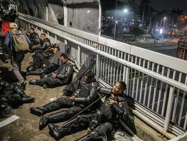 Aparat kepolisan melepas lelah di jembatan penyeberangan orang (JPO) depan Gedung DPR, Jakarta, Selasa (24/9/2019). Mereka melepas lelah usai mengawal demonstrasi mahasiswa menolak pengesahan RUU KUHP dan revisi UU KPK. (Liputan6.com/Faizal Fanani)