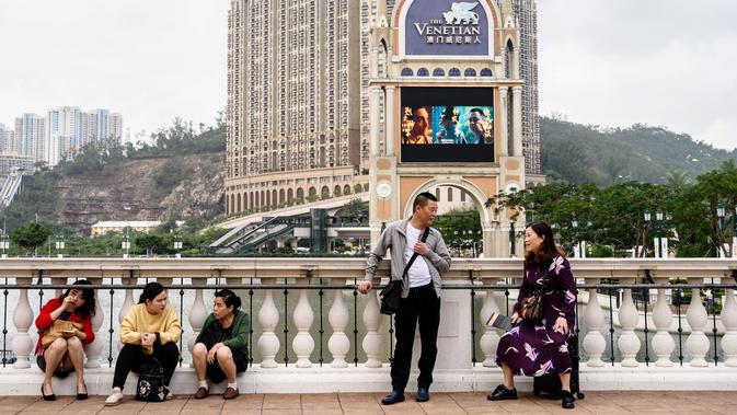 Wisatawan bersantai di sebuah jembatan dengan latar belakang resor kasino The Venetian di Macau, 5 Maret 2019. Macau masuk dalam daerah administrasi khusus di daratan China. (Anthony Wallace/AFP)