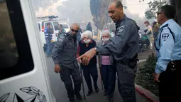 Petugas polisi membantu mengevakuasi sejumlah lansia di kota utara Israel, Haifa, Kamis (24/11). Sekitar 80 ribu warga dievakuasi dan terpaksa meninggalkan rumah mereka akibat kebakaran hutan yang melanda seluruh wilayah tersebut. (REUTERS/Baz Ratner)