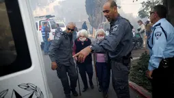 Petugas polisi membantu mengevakuasi sejumlah lansia di kota utara Israel, Haifa, Kamis (24/11). Sekitar 80 ribu warga dievakuasi dan terpaksa meninggalkan rumah mereka akibat kebakaran hutan yang melanda seluruh wilayah tersebut. (REUTERS/Baz Ratner)