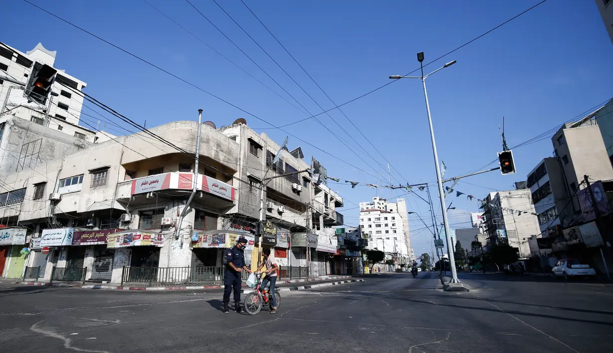 Petugas keamanan Palestina menghentikan pemuda yang mengendarai sepeda pada awal pemberlakukan lockdown total selama 48 jam di Kota Gaza, Selasa (25/8/2020). Lockdown dan jam malam diberlakukan menyusul terkonfirmasinya kasus Covid-19 pertama kalinya di sebuah kamp pengungsian. (MOHAMMED ABED/AFP)