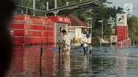 Dua orang pria melintasi area SPBU yang terendam banjir rob akibat naiknya permukaan air laut di Muara Baru, Penjaringan, Jakarta Utara, Kamis (7/12). Banjir rob juga merendam ratusan rumah warga di Muara Baru dan Luar Batang. (Liputan6.com/Johan Tallo)