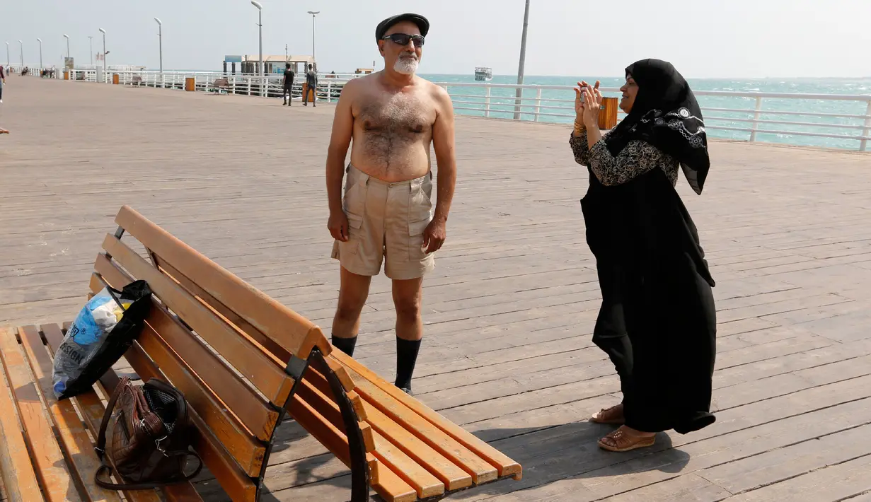 Seorang istri mengambil gambar suaminya di tepi laut, Pulau Kish di Iran, 1 November 2016. Di sini, laki-laki masih diperbolehkan mengenakan celana pendek dan jarang terlihat ada polisi syariat. (Atta Kenare/AFP)