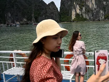 Wisatawan domestik berpose untuk foto di atas kapal di tengah Ha Long Bay, Quang Ninh, Vietnam, (16/5/2020). Sempat terpukul akibat pandemi virus corona Covid-19, pariwisata Vietnam kembali menggeliat setelah otoritas setempat melonggarkan pembatasan perjalanan. (AFP/Manan Vatsyayana)