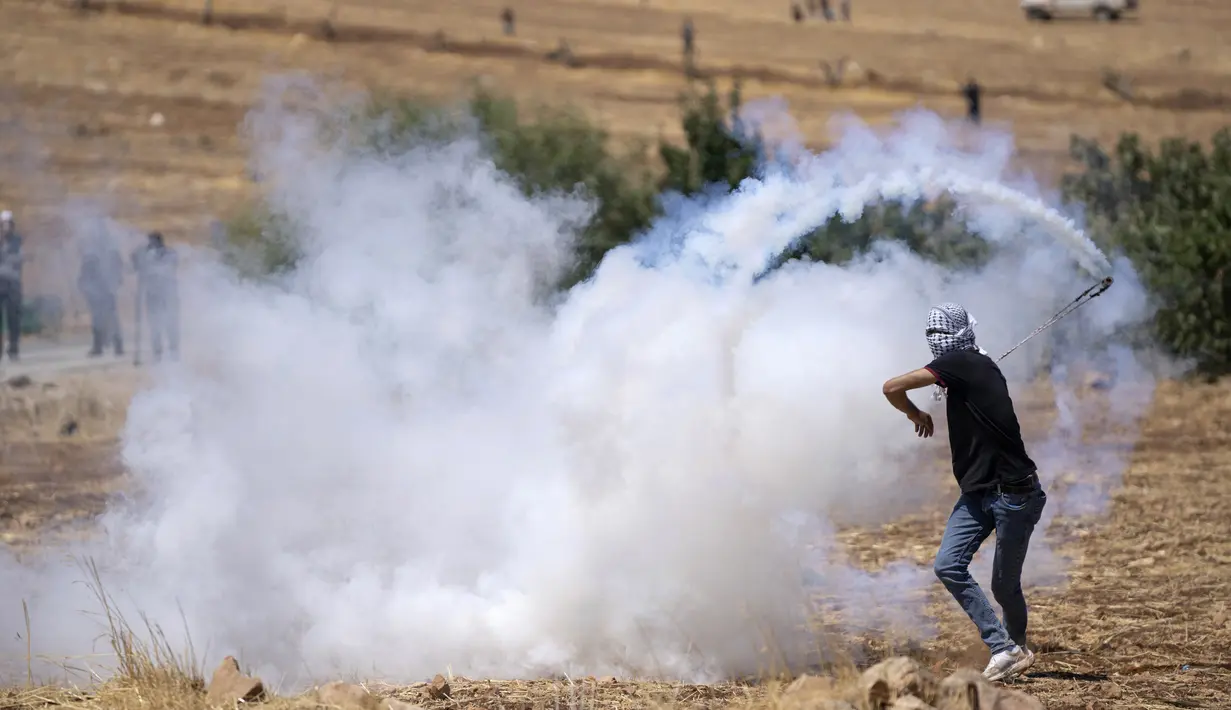Seorang pengunjuk rasa Palestina mengembalikan tabung gas air mata yang ditembakkan tentara Israel untuk membubarkan pengunjuk rasa saat membakar ban dan memblokir jalan yang melewati Desa Mughayer, Tepi Barat, utara Ramallah, 29 Juli 2022. Warga Palestina yang memprotes aktivitas permukiman Israel memblokir jalan utama dan bentrok dengan pemukim Israel, sementara tentara menembakkan gas air mata untuk membubarkan mereka. (AP Photo/Nasser Nasser)