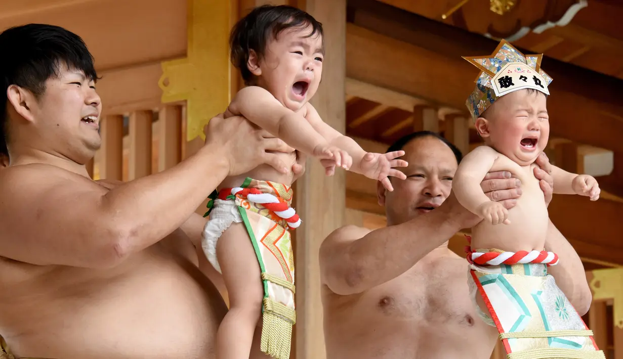 Dua pesumo menggendong bayi yang menangis selama Festival Nakizumo di kuil Kamegaike-Hachiman, Jepang, Minggu (14/5). Bayi yang menangis dengan suara keras dan lantang akan terpilih sebagai pemenang kontes bayi menangis. (Toru YAMANAKA/AFP)