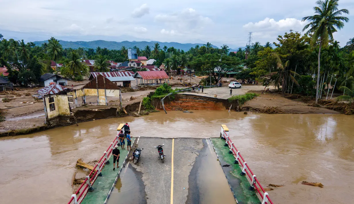 Selain jembatan yang putus, banjir juga merendam ratusan rumah warga di sepanjang aliran sungai Meureudu. Tampak foto udara menunjukkan jembatan yang rusak akibat banjir bandang di jalan utama yang menghubungkan Aceh dan Sumatera Utara di Meureudu, Kabupaten Pidie Jaya, Provinsi Aceh, pada Jumat 28 November 2025. (CHAIDEER MAHYUDDIN/AFP)
