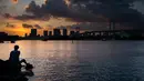 Seorang pria berada di samping The Rainbow Bridge saat matahari terbenam di Tokyo, Jepang (29/7). Odaiba merupakan salah satu tujuan wisata di Tokyo, sekaligus lokasi pusat perbelanjaan dan permukiman. (AFP Photo/Martin Bureau)