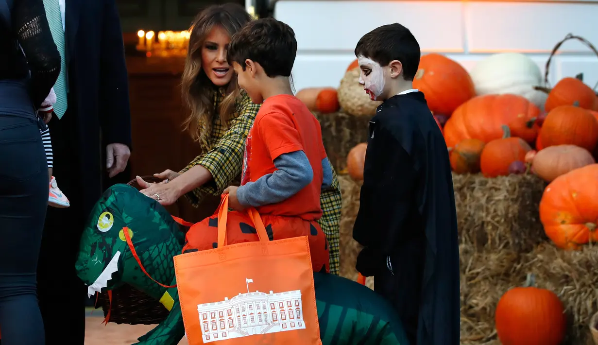 First lady Melania Trump menyapa anak berkostum dinosaurus ketika dirinya dan Presiden AS Donald Trump memberikan permen selama yang hadir acara trick-or-treat pada perayaan Halloween di Gedung Putih, Washington, Minggu (28/10). (AP/Jacquelyn Martin)