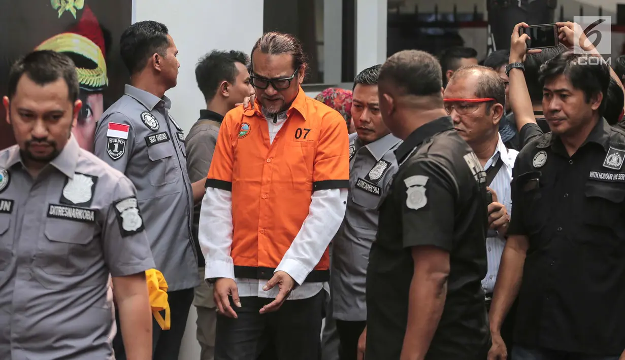Suami komedian Tri Retno Prayudati alias Nunung, July Jan Sambiran digiring petugas saat dihadirkan dalam rilis kasus narkoba di Polda Metro Jaya, Jakarta, Senin (22/7/2019). July Jan Sambiran dan Nunung ditangkap usai bertransaksi narkoba. (Liputan6.com/Faizal Fanani)