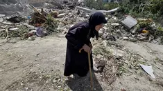 Seorang wanita lanjut usia berjalan melewati petugas pertahanan sipil Lebanon yang sedang mencari korban di antara reruntuhan, sehari setelah serangan Israel di desa Deir Qanun al-Nahr, Lebanon Selatan, pada Rabu 20 Mei 2026. (KAWNAT HAJU/AFP)