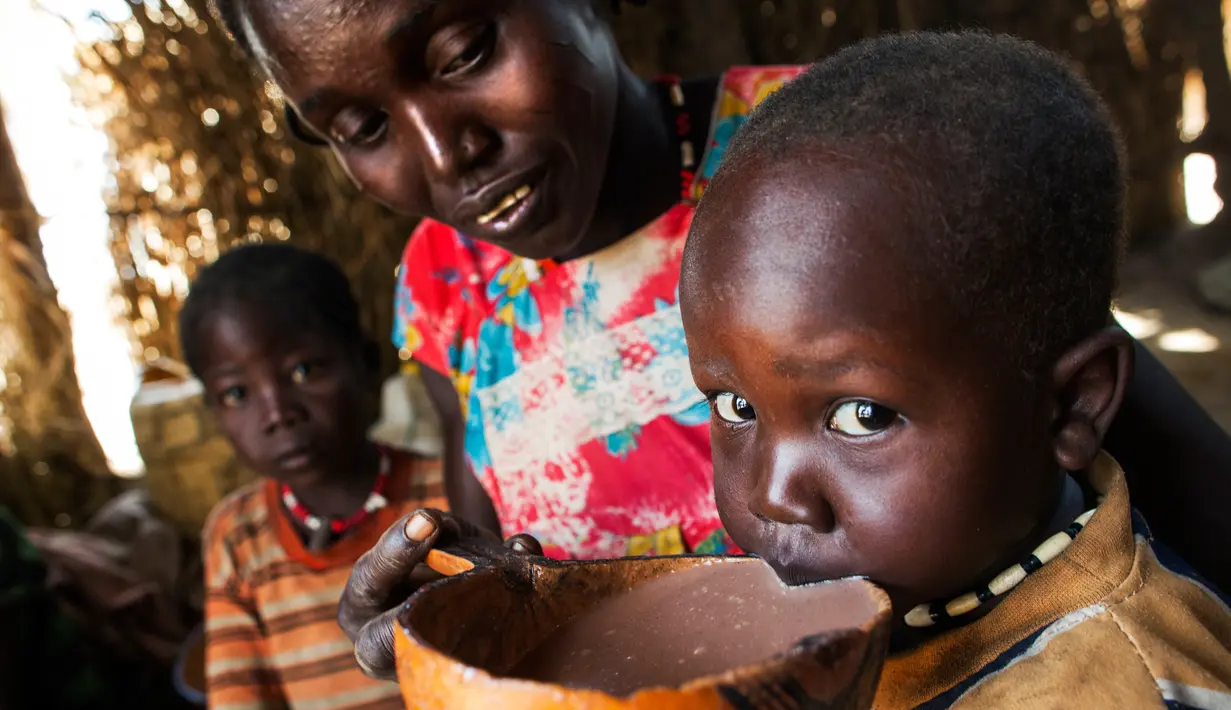 Seorang wanita bernama Nybol Madut memberi minum semangkuk alkohol lokal kepada anaknya di tempat penampungan di Sudan Selatan (22/11). (AFP Photo/Albert Gonzalez Farran)