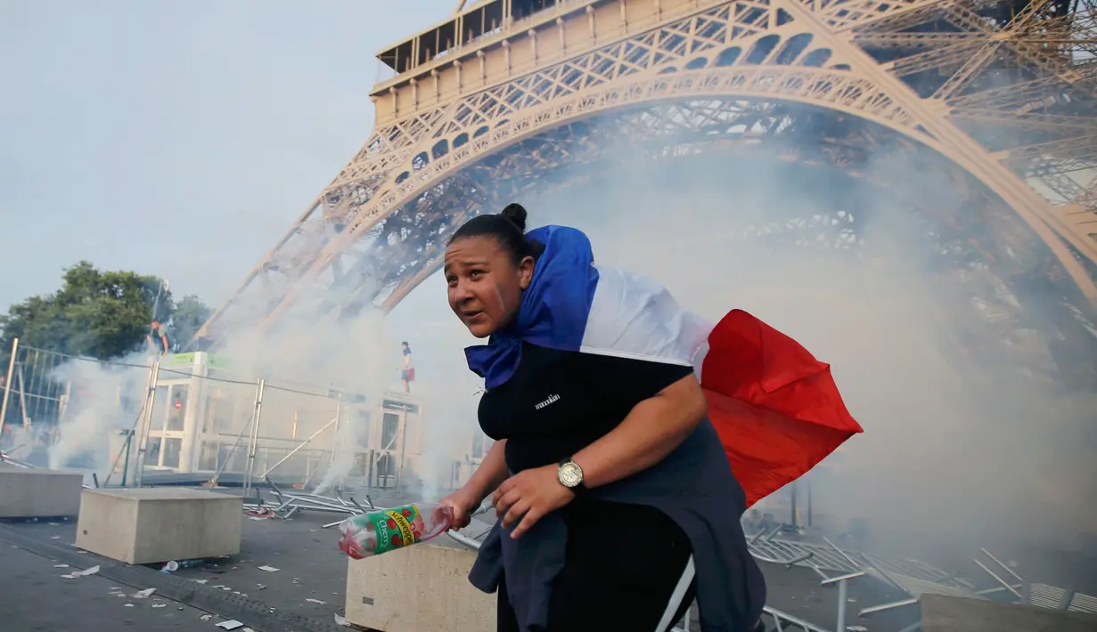 Seorang demonstran berlari menghindari gas air mata yang ditembakan polisi di bawah Menara Eiffel di dekat zona penggemar Paris sebelum laga Portugal vs Prancis di Final EURO 2016 di Prancis (10/6). (REUTERS/Stephane Mahe)