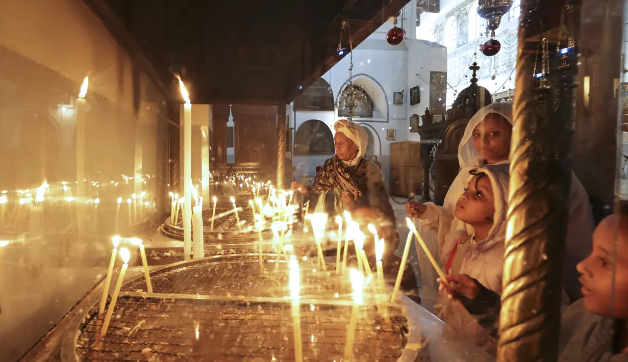 Peziarah dan turis menyalakan lilin menjelang Natal di dalam Gereja Kelahiran Yesus di kota Bethlehem, Tepi Barat pada 22 Desember 2022. Beberapa tempat indah yang diincar pengunjung menyambut Natal di Kota Bethlehem adalah Gereja Kelahiran yang sudah berusia ratusan tahun. (AFP/Hazem Bader)