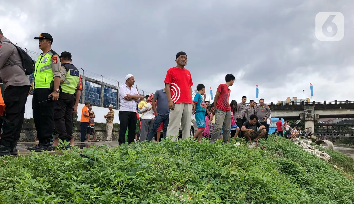 Warga bersama personel kepolisian, Satpol PP, dan TNI berkumpul di bantaran Sungai Ciliwung, Jakarta, Selasa (25/2/2020). Adanya warga yang hanyut saat berenang di tengah luapan Sungai Ciliwung mengundang perhatian warga dan petugas yang mencari keberadannya. (Liputan6.com/Immanuel Antonius)