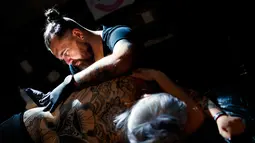 Seorang seniman  mentato badan pengunjung wanita dalam acara edisi keempat Montreux Tattoo Convention di Montreux, Swiss  (22/9). Montreux Tattoo Convention berlangsung selama tiga hari. (Valentin Flauraud/Keystone via AP)