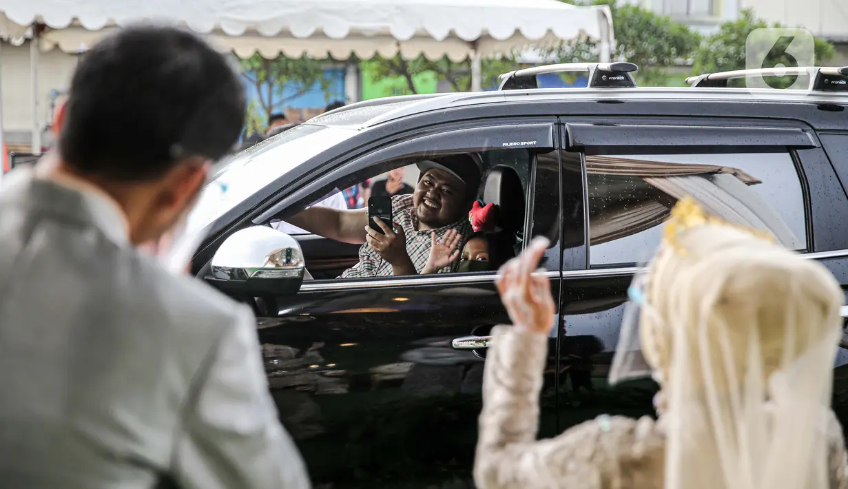 Tamu undangan menyapa pasangan mempelai pada acara resepsi pernikahan secara "drive thru" di Bekasi, Jawa Barat, Sabtu (8/8/2020). Resepsi pernikahan secara drive thru menjadi alternatif pesta pernikahan guna mencegah penyebaran wabah COVID-19. (Liputan6.com/Faizal Fanani)