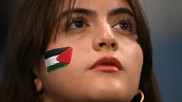 Suporter wanita mengenakan cat wajah sesaat sebelum pertandingan sepak bola Grup C Piala Asia AFC Qatar 2023 antara Palestina dan Uni Emirat Arab di Stadion Al-Janoub di Al-Wakrah, Doha pada 18 Januari 2024. (HECTOR RETAMAL/AFP)