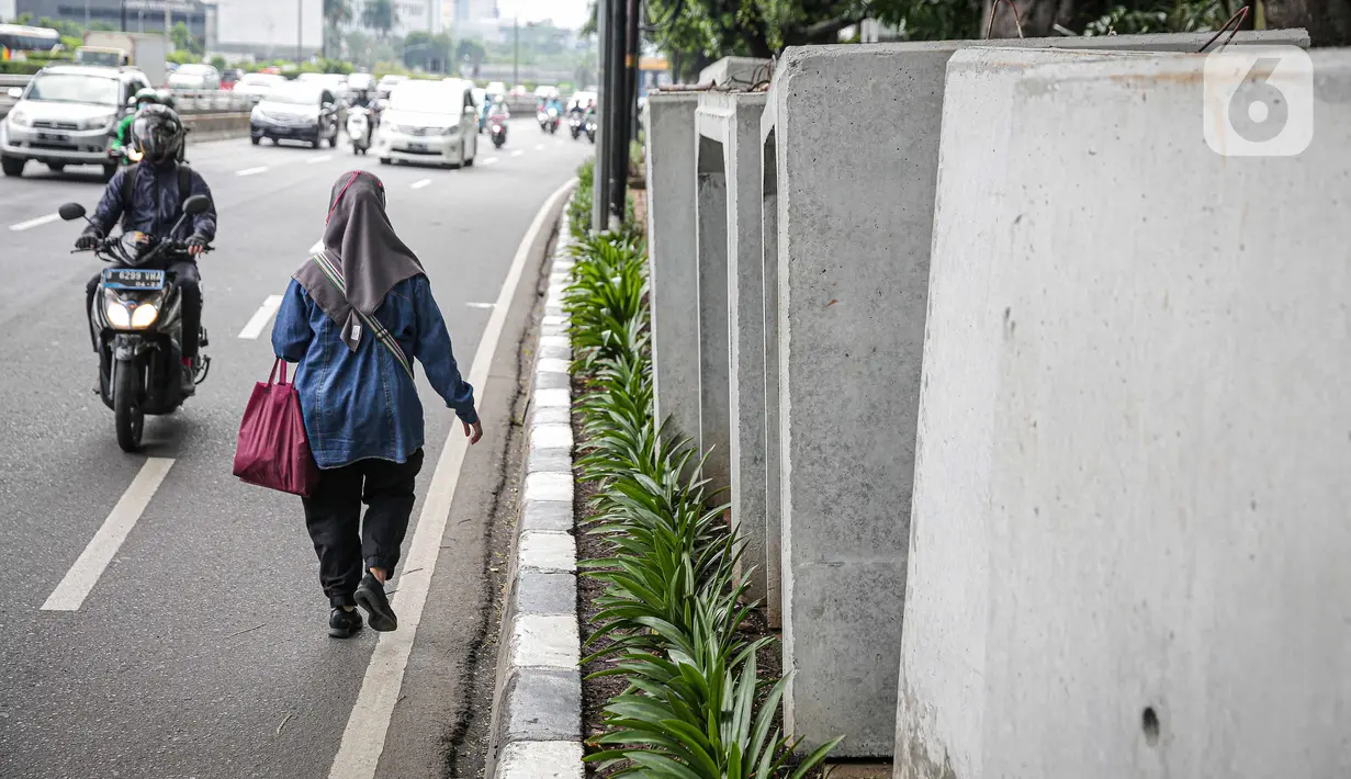 Pejalan kaki melintas di samping beton saluaran air yang berada di jalur pedestrian kawasan Gatot Subroto, Jakarta, Selasa (21/12/2021). Selain mengganggu kenyamanan, keberadaan beton saluran air tersebut juga dapat membahayakan pejalan kaki yang melintas. (Liputan6.com/Faizal Fanani)