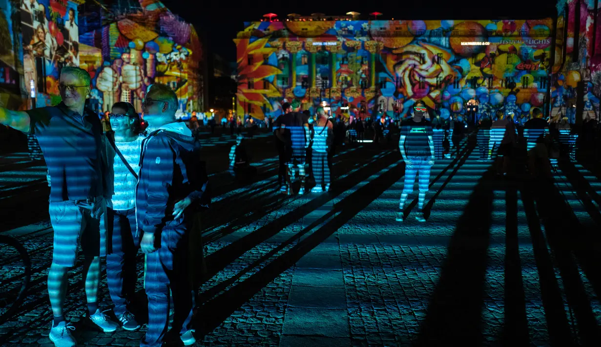 Orang-orang mengambil foto saat mengunjungi Bebel platz yang diterangi cahaya dalam Festival of Lights di Berlin pada 14 September 2020. Kreasi cahaya lebih dari 90 karya seni tersebut ditampilkan di 86 lokasi yang berlangsung hingga 20 September mendatang. (John MACDOUGALL/AFP)