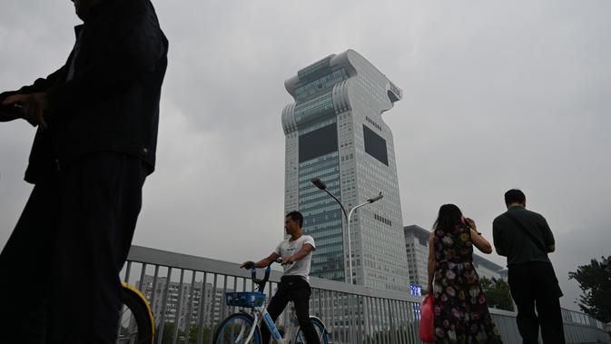 Orang-orang melewati gedung pencakar langit Pangu Plaza di seberang Stadion Olimpiade Bird's Nest, Beijing, Selasa (20/7/2019). Gedung yang pernah masuk dalam film Transformers: Age of Extinction itu terjual dalam lelang online dengan harga 734 juta USD atau sekitar Rp10,5 triliun. (GREG BAKER/AFP)